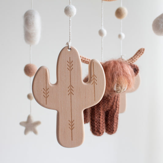Close up of a wooden cactus (approx. 10 cm tall) with engraved arrows, hanging from a mobile with other elements.