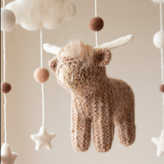 Close-up of a hand-knitted highland cow with fuzzy texture and neutral yarn horns for a farm nursery.