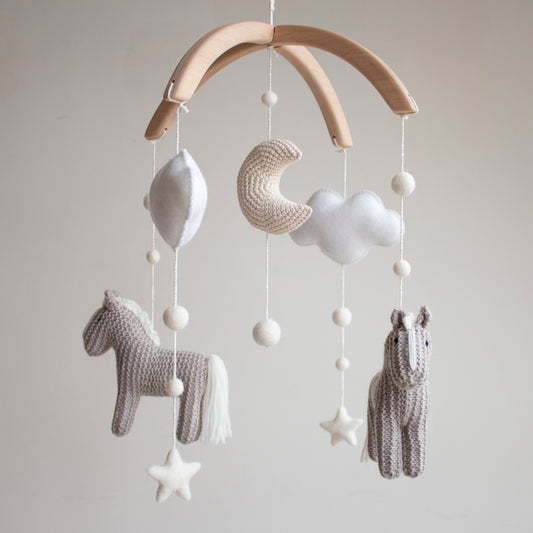 Macro view of 100% wool yarn stitches on a handmade horse baby mobile. Untreated solid alder wood cross-arch hanger for a minimalist artisan baby mobile.