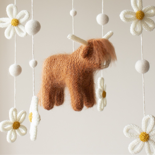 Close-up of a knitted highland cow in rust with fuzzy texture and neutral yarn horns.