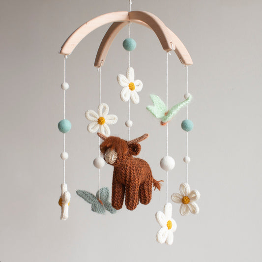 Hand-knitted dark brown highland cow mobile with high-contrast white flowers and light butterflies to support newborn visual development.
