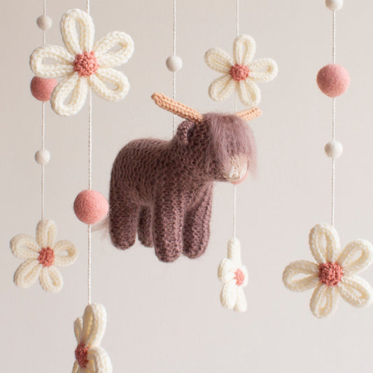 Close-up of a knitted highland cow in cocoa brown with fuzzy texture and neutral yarn horns. Macro view of 100% wool-mix yarn stitches on a handmade highland cow baby gift.