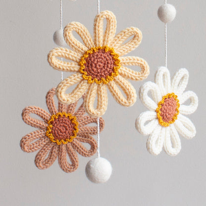 Close-up of a hand-knitted sunflower with a brown textured center and golden yellow wool petals. Detail of 100% wool yarn stitches on a handmade sunshine-themed baby gift.