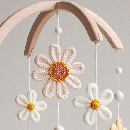 Macro view of small white crochet daisies and wool felt balls on a floral baby mobile.