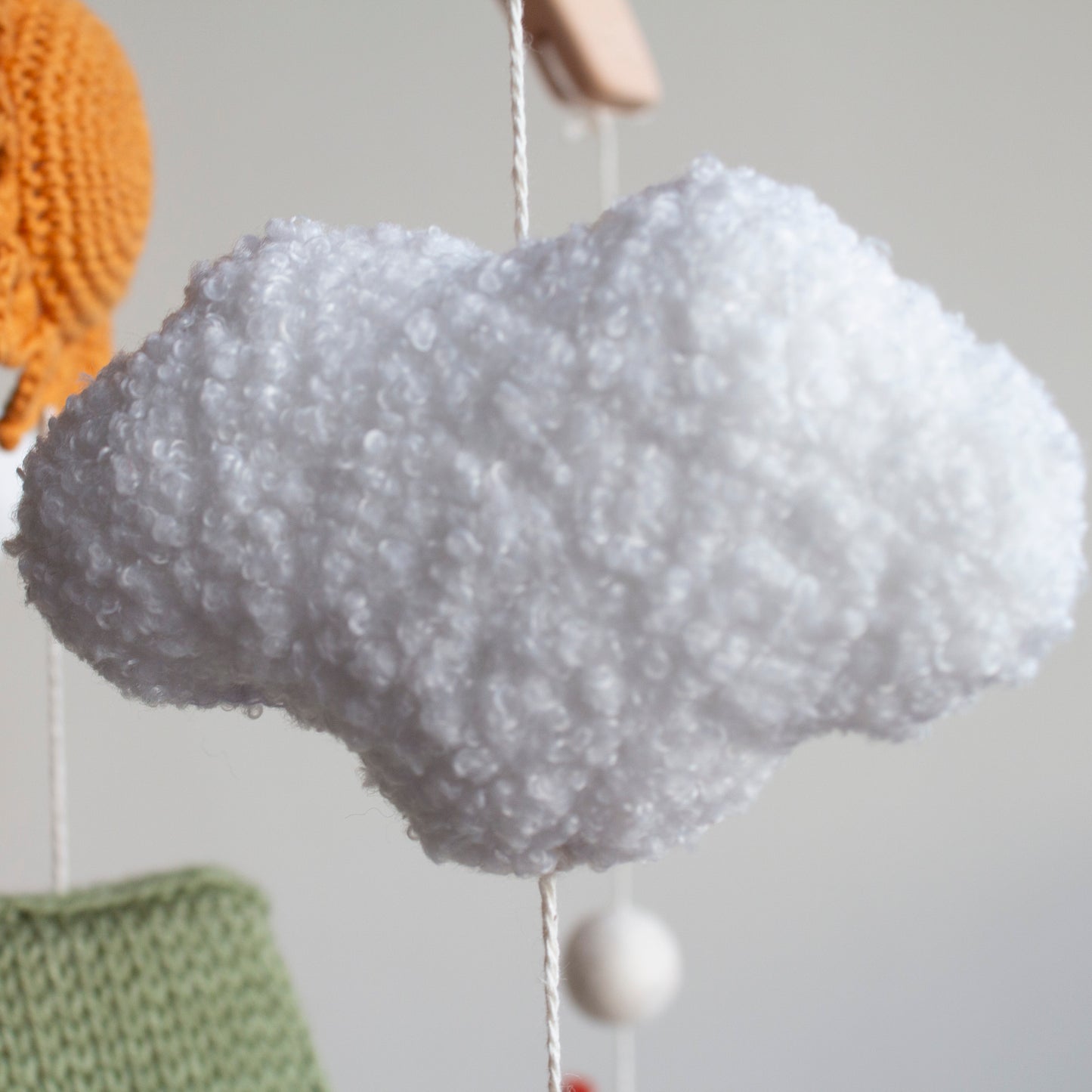 Fluffy white bouclé clouds and earthy-toned wool balls on a baby mobile.