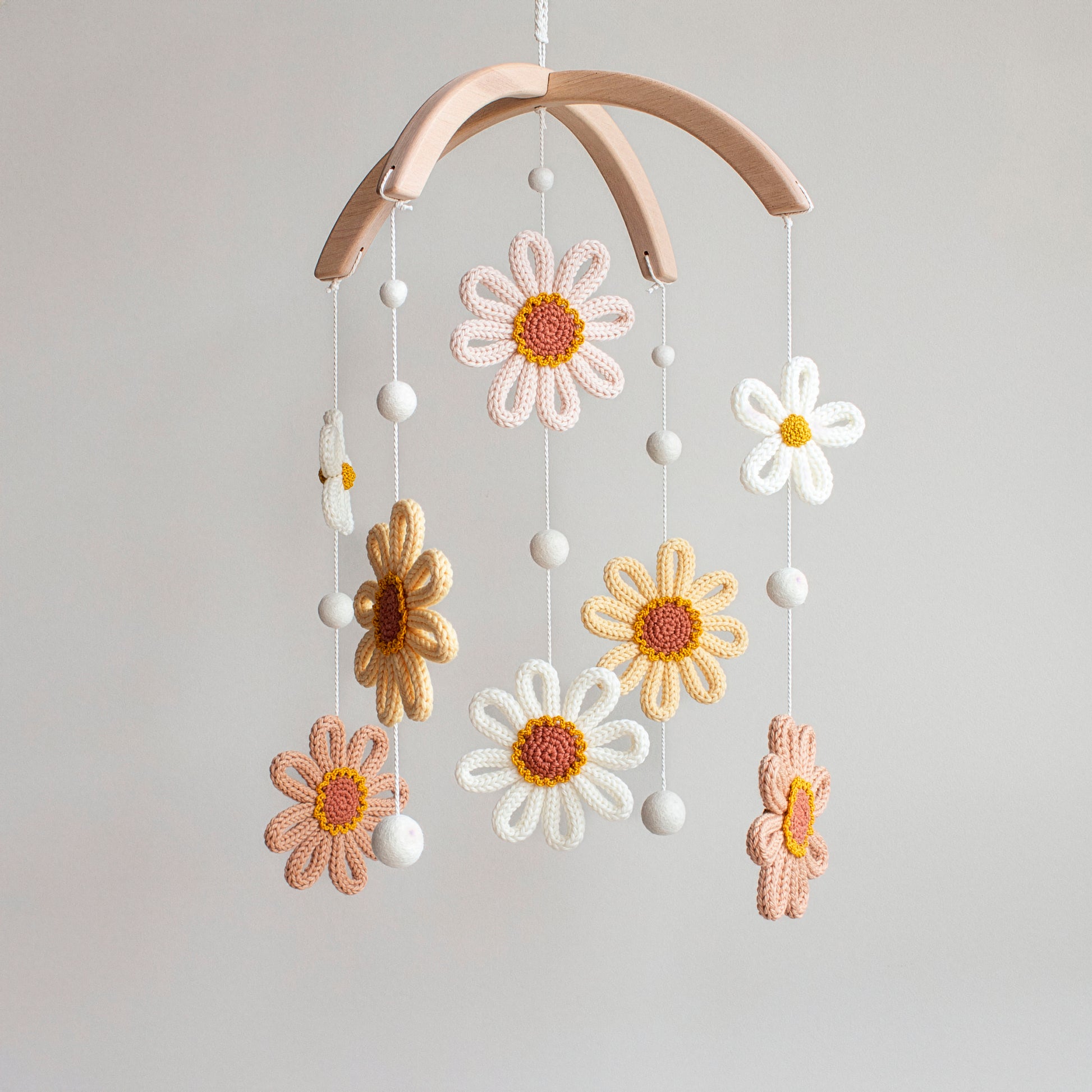 Hand-knitted sunflower baby mobile with yellow petals and white daisies on a wooden hanger.