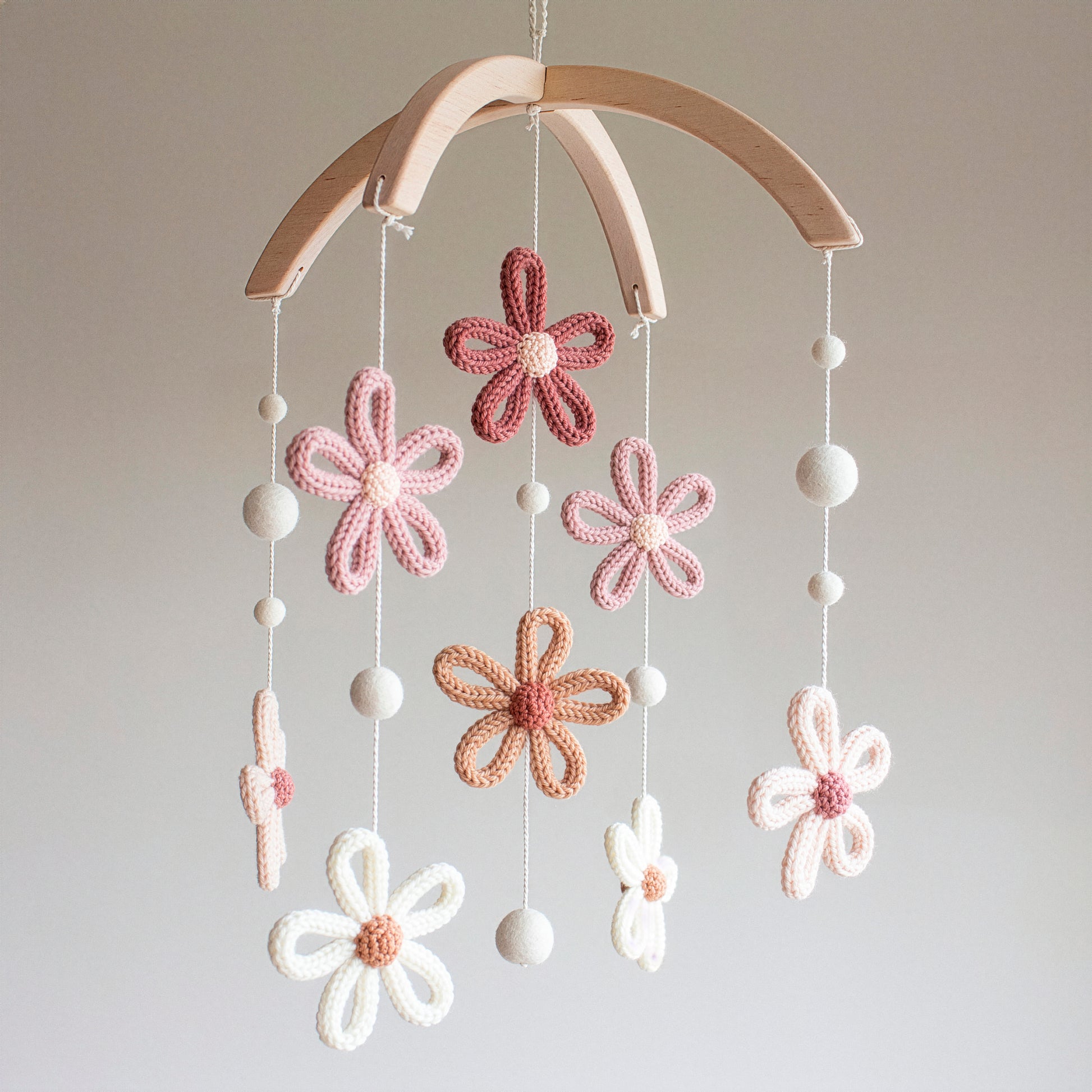 A beautiful baby mobile featuring five crochet flowers in earthy tones hanging from a natural wood frame. The design uses premium wool yarn certified to OEKO-TEX Standard 100, ensuring it is safe for newborns and sensitive skin. Crafted with untreated solid wood, this mobile offers a timeless design that fits perfectly in a minimalist or boho nursery. It serves as a high-quality heirloom gift or a thoughtful choice for baby shower gifts, providing gentle visual stimulation for infants.