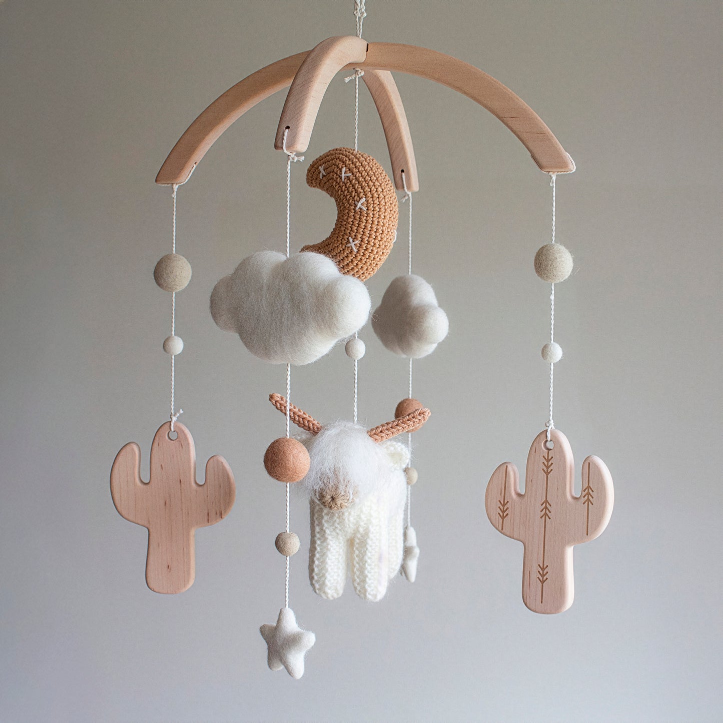 A full view of the White Longhorn Cow Mobile, showcasing the meticulous craftsmanship of the tan moon and shaggy "hairy coo." The mobile uses wool yarn OEKO-TEX Standard 100 safe for infants and features smooth, untreated solid alder wood cactuses. This timeless design creates a serene focal point in any nursery. As a durable heirloom gift, it is a thoughtful choice suitable for different baby gifts, including baby showers and "welcome home" presents for new parents.