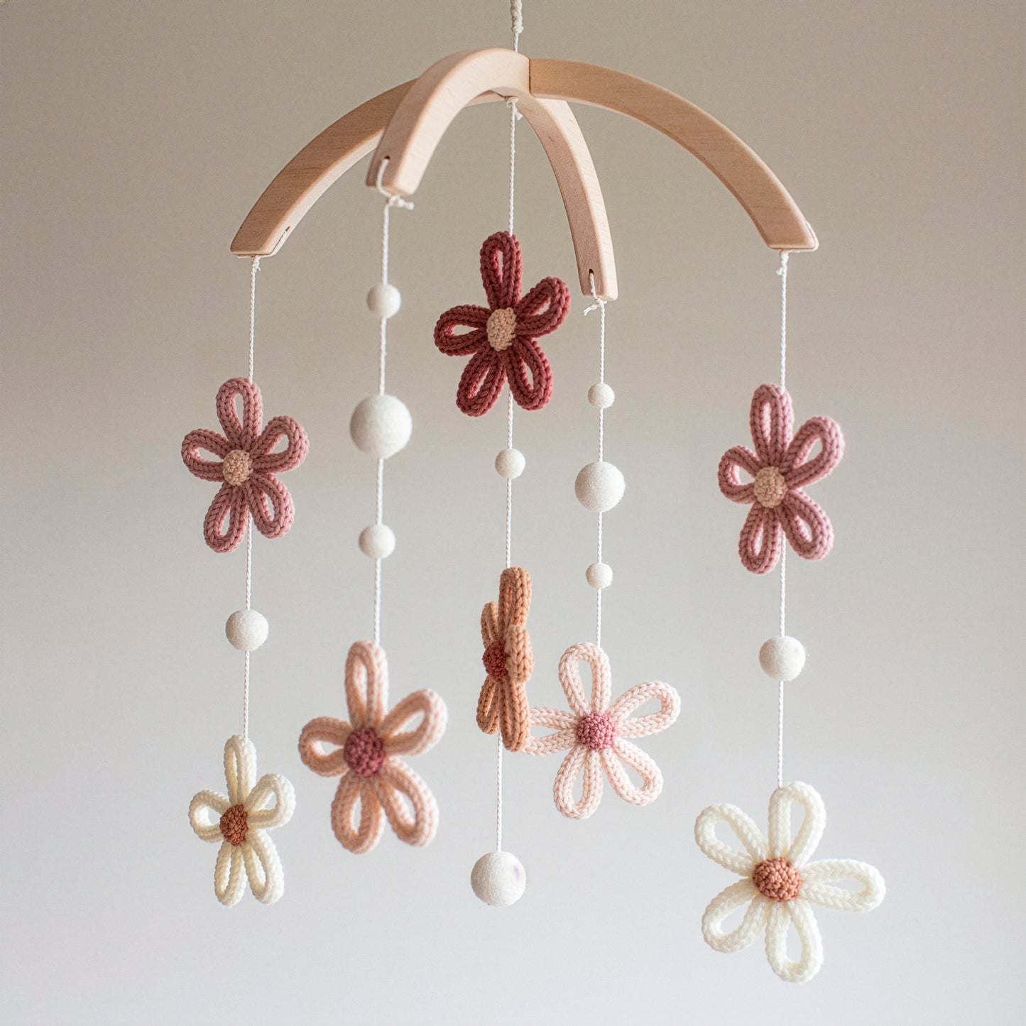A detailed view of a floral baby mobile featuring crochet daisies in warm autumnal tones like rust, peach, and ivory. The mobile is crafted from wool yarn OEKO-TEX Standard 100 safe for little ones and hangs from a sturdy, untreated solid wood frame. Its timeless design ensures it remains a stylish nursery staple for years. Ideal as a meaningful heirloom gift, it is also suitable for different baby gifts such as "welcome home" presents or high-end registry items for new parents.