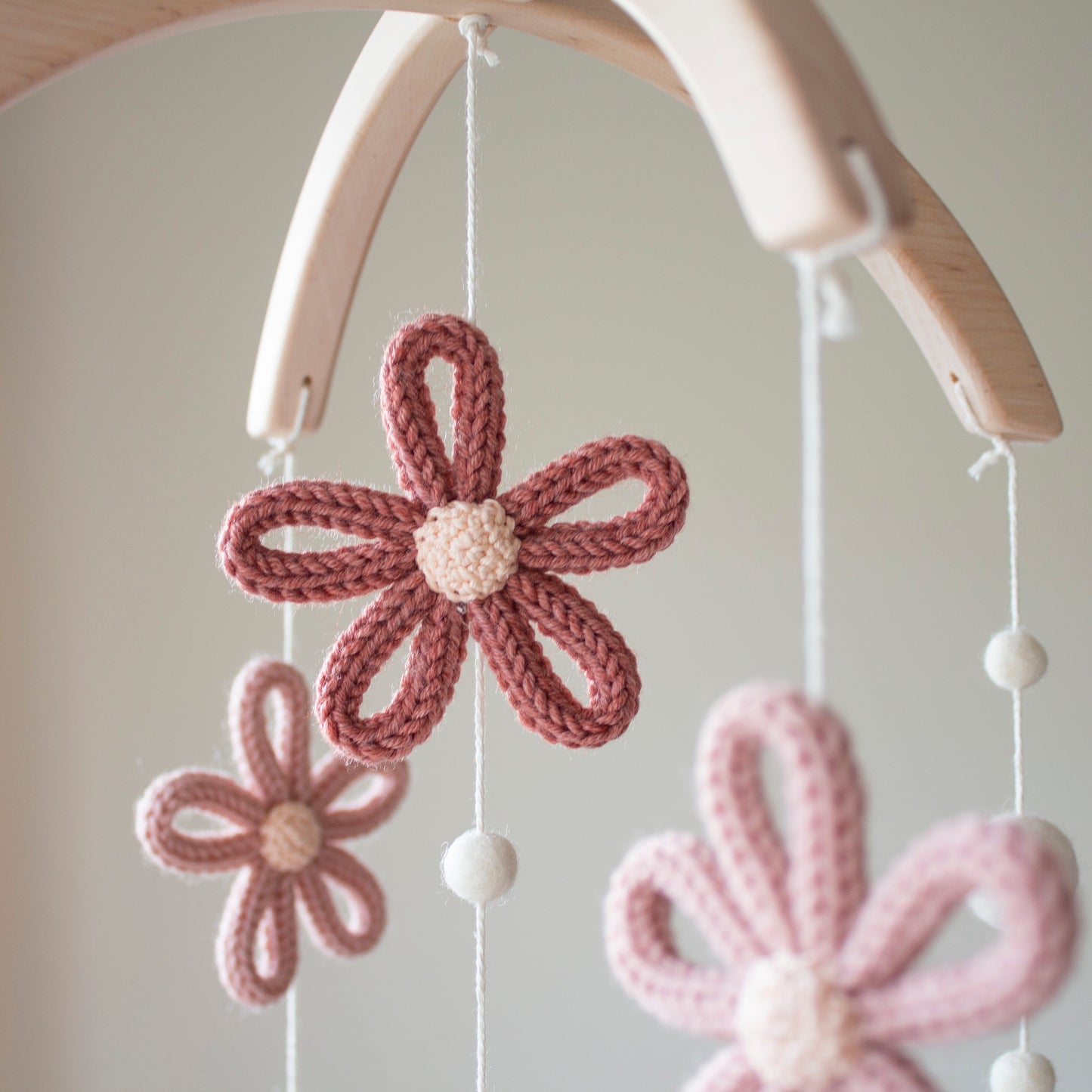 A close-up view focusing on a deep terracotta crochet flower with a cream center, part of a handmade baby mobile. The intricate knit texture is created with wool yarn OEKO-TEX Standard 100 safe for infants, guaranteeing no harmful substances. Paired with untreated solid wood accents, the mobile boasts a timeless design. This piece is perfect for those looking for an heirloom gift that symbolizes quality craftsmanship and is suitable for different baby gifts and celebrations.