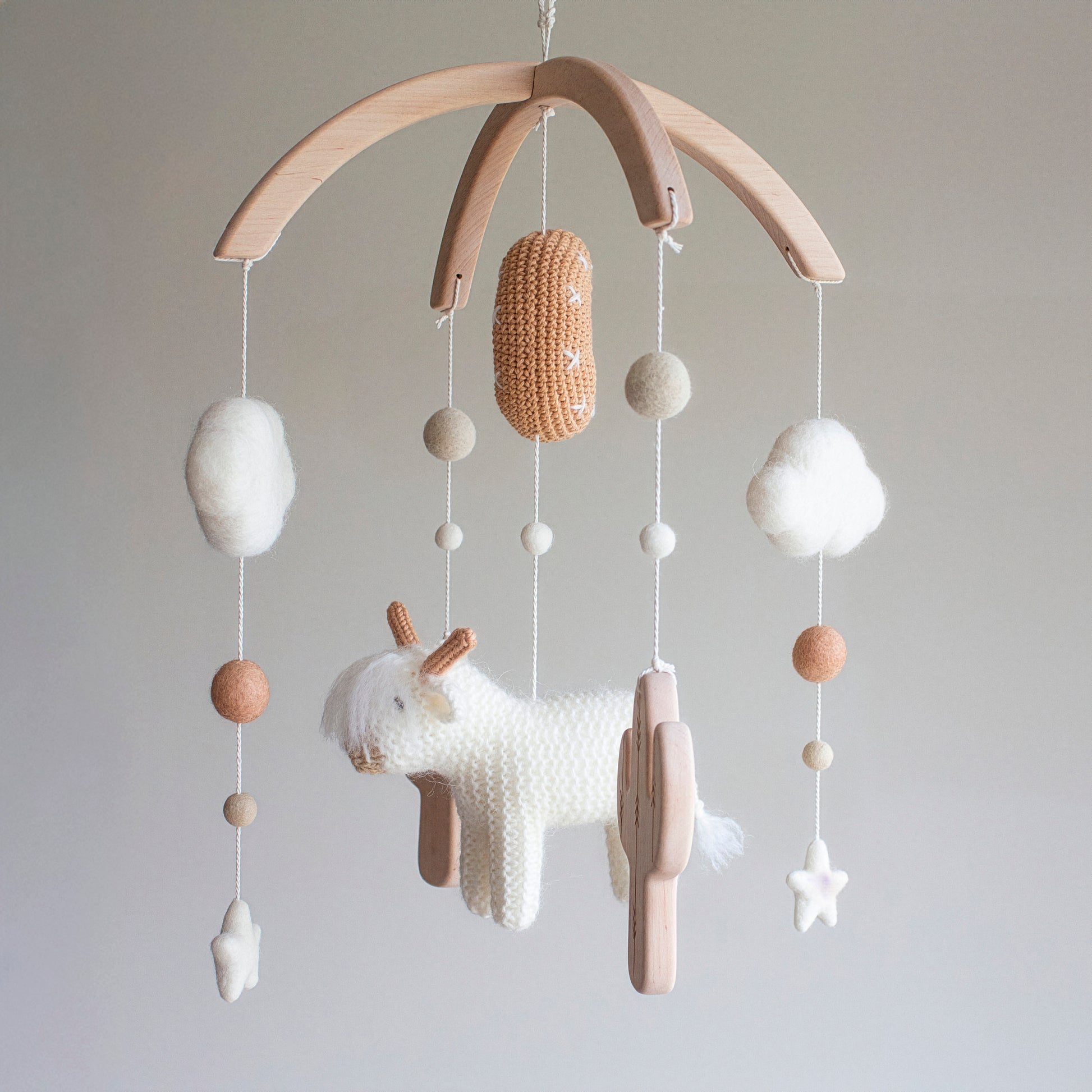 Capturing the spirit of the open range, this desert-themed mobile features a hand-knitted white cow and stars. Every element is crafted using premium wool yarn OEKO-TEX Standard 100 safe for children and hung from an untreated solid wood mobile frame. The architectural lines of the untreated solid wood cactuses add a rustic touch. This piece is a one-of-a-kind heirloom gift with a timeless design, making it highly suitable for different baby gifts for a Scandi-style home.