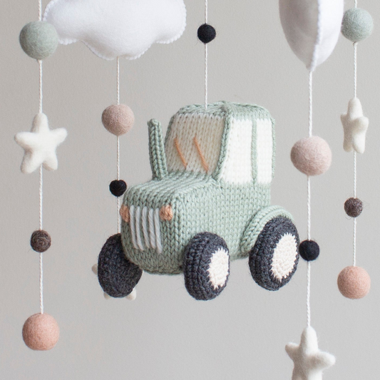 Close-up of a hand-knitted sage green tractor with black wheels and cream window detailing for a farm nursery.