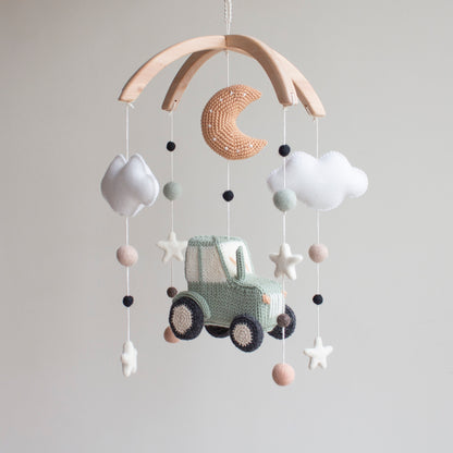 Hand-knitted sage green tractor baby mobile with white clouds and crochet moon on a wooden arch.