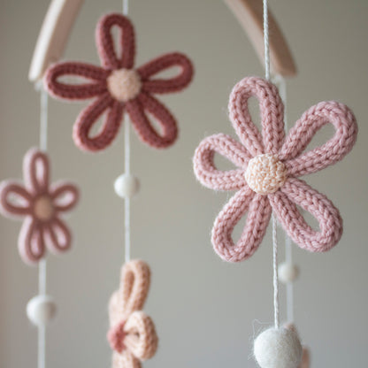 Close-up of a dusty pink crochet daisy and white felted wool balls on a nursery mobile. The soft texture of the wool yarn OEKO-TEX Standard 100 safe for babies provides a tactile and soothing aesthetic. Supported by a frame of untreated solid wood, this mobile exemplifies a timeless design that complements any nursery decor. It is a wonderful choice for an heirloom gift, and its high-quality materials make it suitable for different baby gifts, from christenings to birthdays.