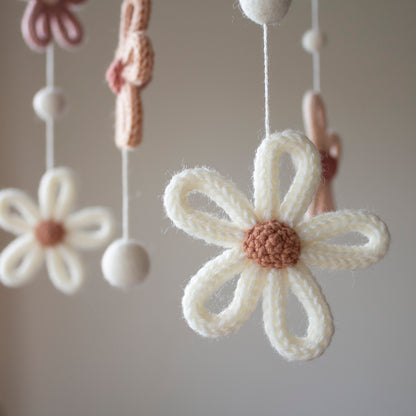 A detailed close-up of a cream-colored knitted flower with a brown center, hanging elegantly on a mobile string. The use of wool yarn OEKO-TEX Standard 100 safe for nurseries ensures a healthy environment for babies. This mobile features untreated solid wood, lending a natural feel to its timeless design. Whether you are looking for a special heirloom gift or are shopping for suitable for different baby gifts, this handmade piece from Lanacrocheting.com offers style and safety.