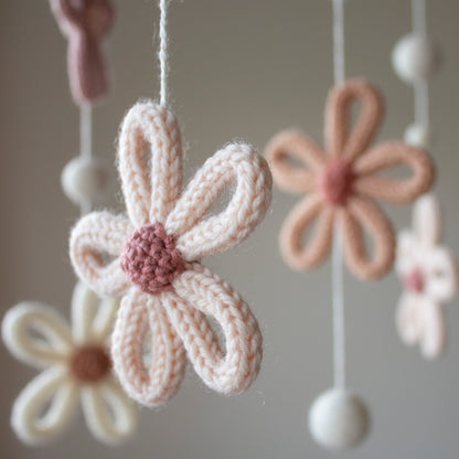 A soft-focus close-up of a peach crochet flower with a rose-colored center. This delicate nursery accessory is handmade with wool yarn OEKO-TEX Standard 100 safe for babies, prioritizing health and quality. The frame is made from untreated solid wood, emphasizing its organic appeal and timeless design. This mobile is designed to be a long-lasting heirloom gift and is highly suitable for different baby gifts, making it a standout addition to any newborn's sleeping space.