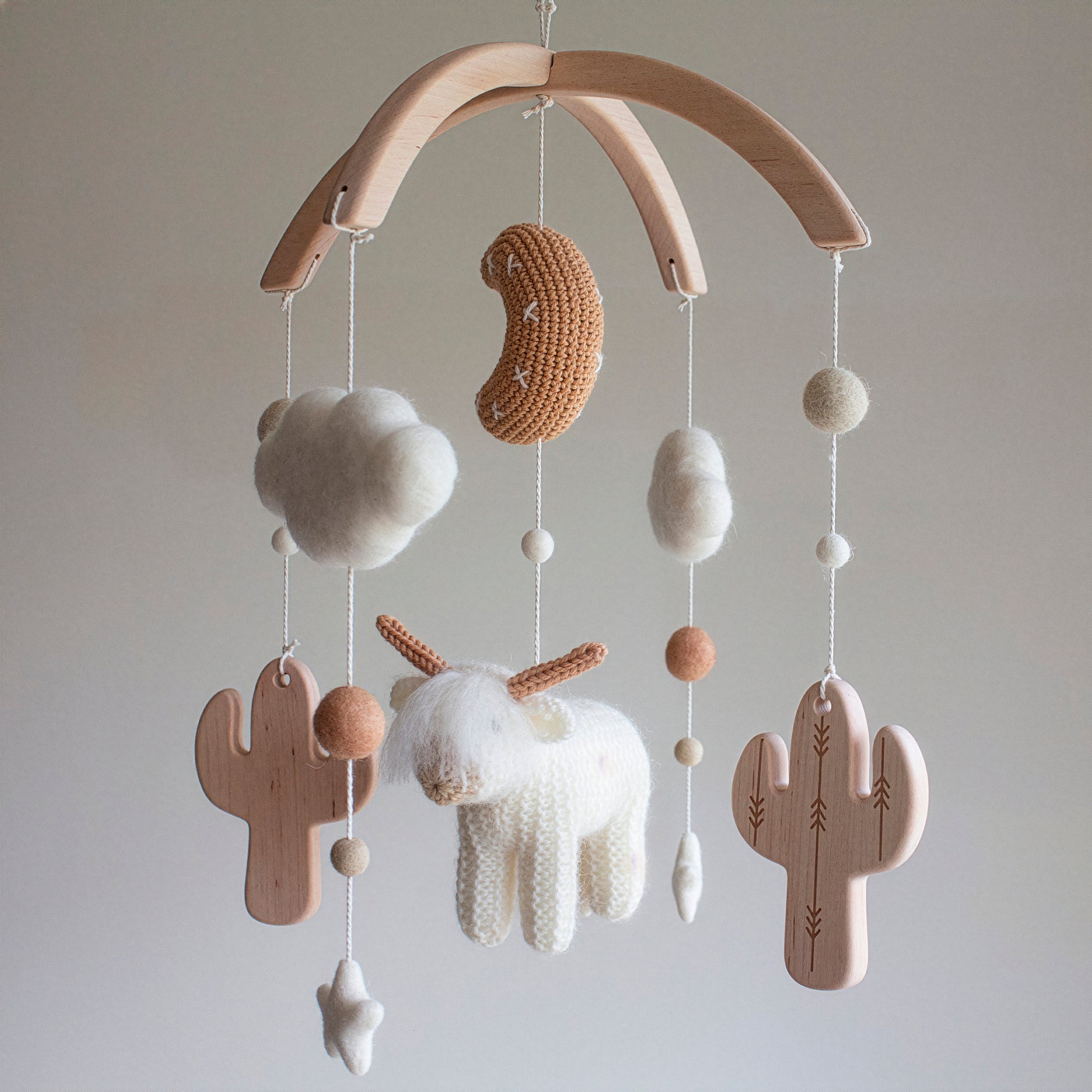 Handmade in the UK, this nursery mobile features a shaggy "floofy" cow and architectural untreated solid wood cactuses. The use of wool yarn OEKO-TEX Standard 100 safe for babies and an untreated solid wood mobile frame ensures a natural, chemical-free nursery. This timeless design acts as a striking statement piece and a durable heirloom gift. Its sophisticated earthy tones make it suitable for different baby gifts, perfect for parents who love minimalist and rustic styles.
