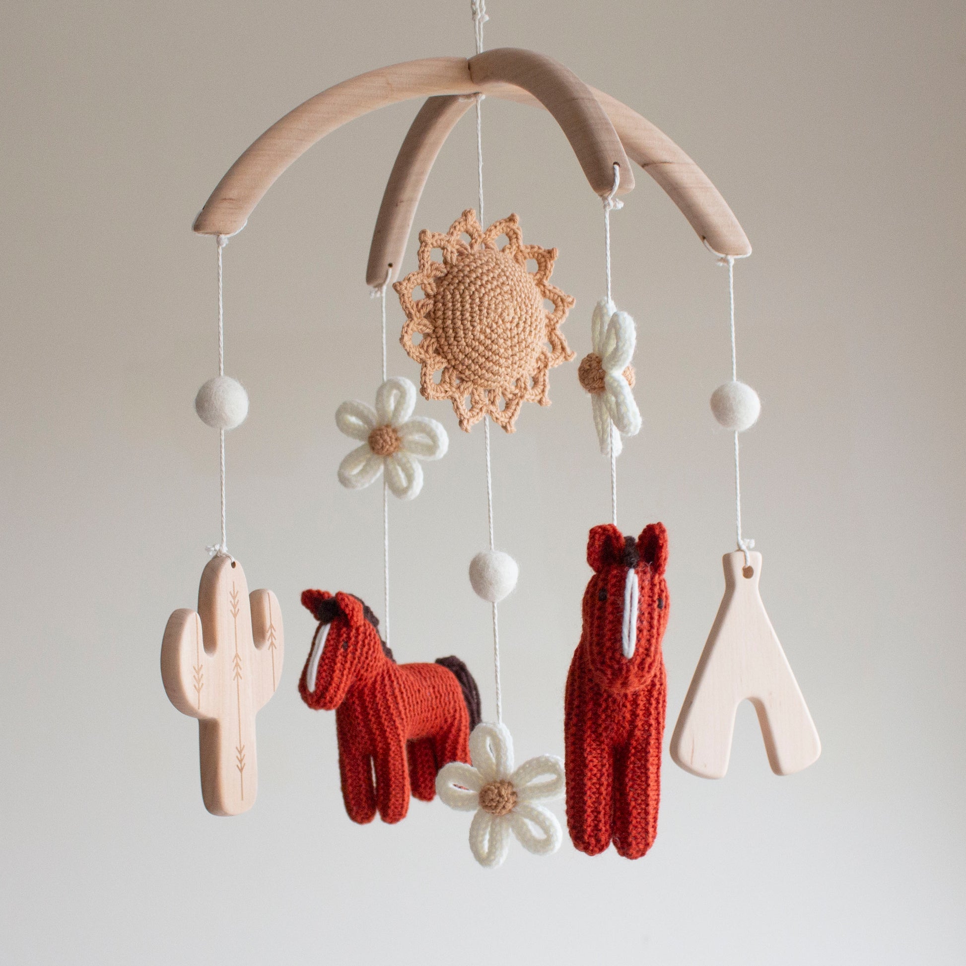 Boho cowgirl nursery mobile showing high-contrast red horses and white floral elements for infant visual stimulation.