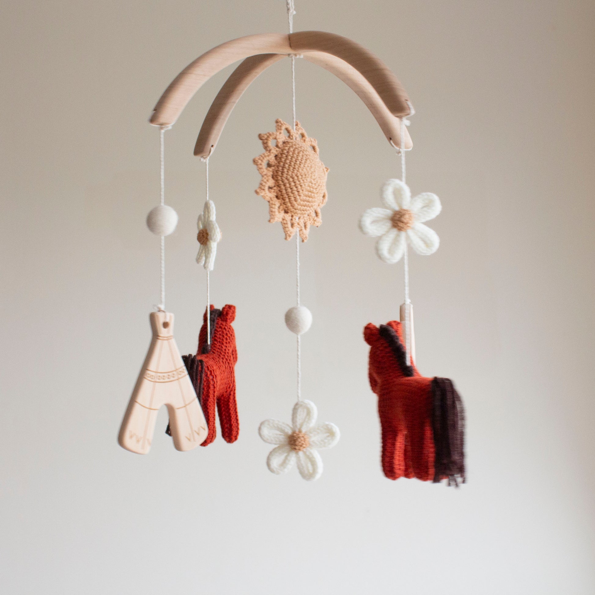 Whimsical floral cowgirl nursery mobile hanging in a modern baby room above a wooden crib.