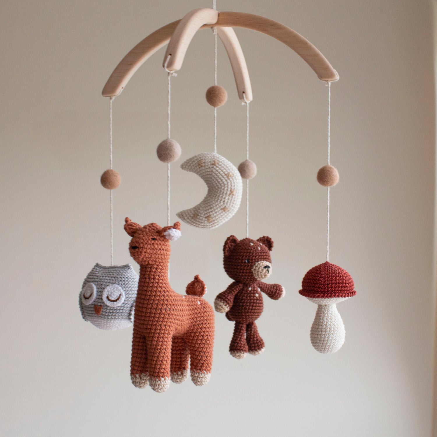 Hand-crocheted forest animal baby mobile with bear, deer, owl, and mushroom on a wooden arch.