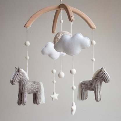 Hand-knitted horse baby mobile with neutral grey ponies, white clouds, and crochet moon on a wooden arch. 
Close-up of a hand-knitted crochet pony in warm grey wool for an equestrian nursery theme.