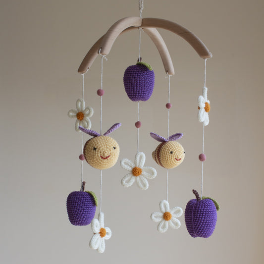 Hand-crocheted bees and plums baby mobile with white daisies on a natural wooden arch.