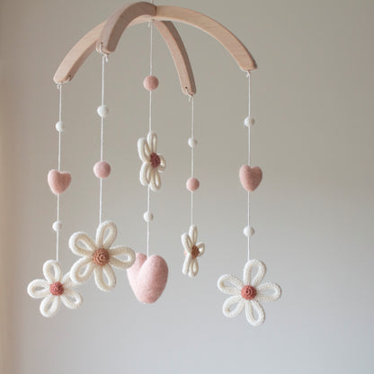 Close-up of knitted daisy petals and felted hearts on a wooden alder wood mobile hanger.