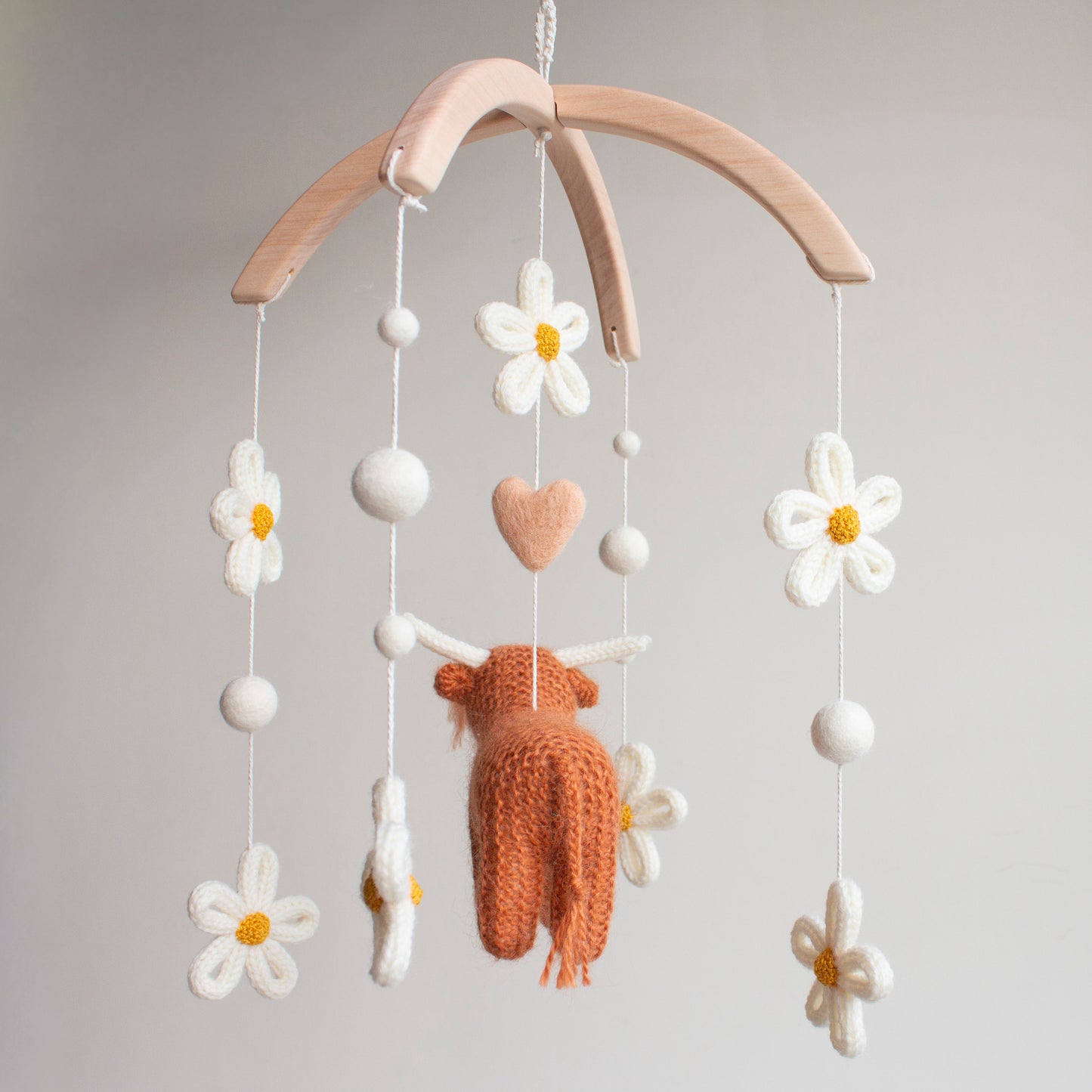 Rear view of a handcrafted heirloom highland cow baby mobile featuring ivory floral accents and a peachy-blush wool heart. Every detail is hand-knitted with care using non-toxic, sustainable materials on a smooth wooden frame. This premium UK nursery decor is designed to be a lasting keepsake. It offers a sophisticated alternative to mass-produced items, perfect for baby registries and thoughtful gifting to friends who value unique, artisan design.