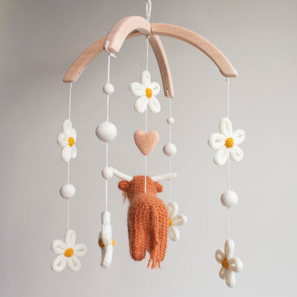 Rear view of a handcrafted heirloom highland cow baby mobile featuring ivory floral accents and a peachy-blush wool heart. Every detail is hand-knitted with care using non-toxic, sustainable materials on a smooth wooden frame. This premium UK nursery decor is designed to be a lasting keepsake. It offers a sophisticated alternative to mass-produced items, perfect for baby registries and thoughtful gifting to friends who value unique, artisan design.
