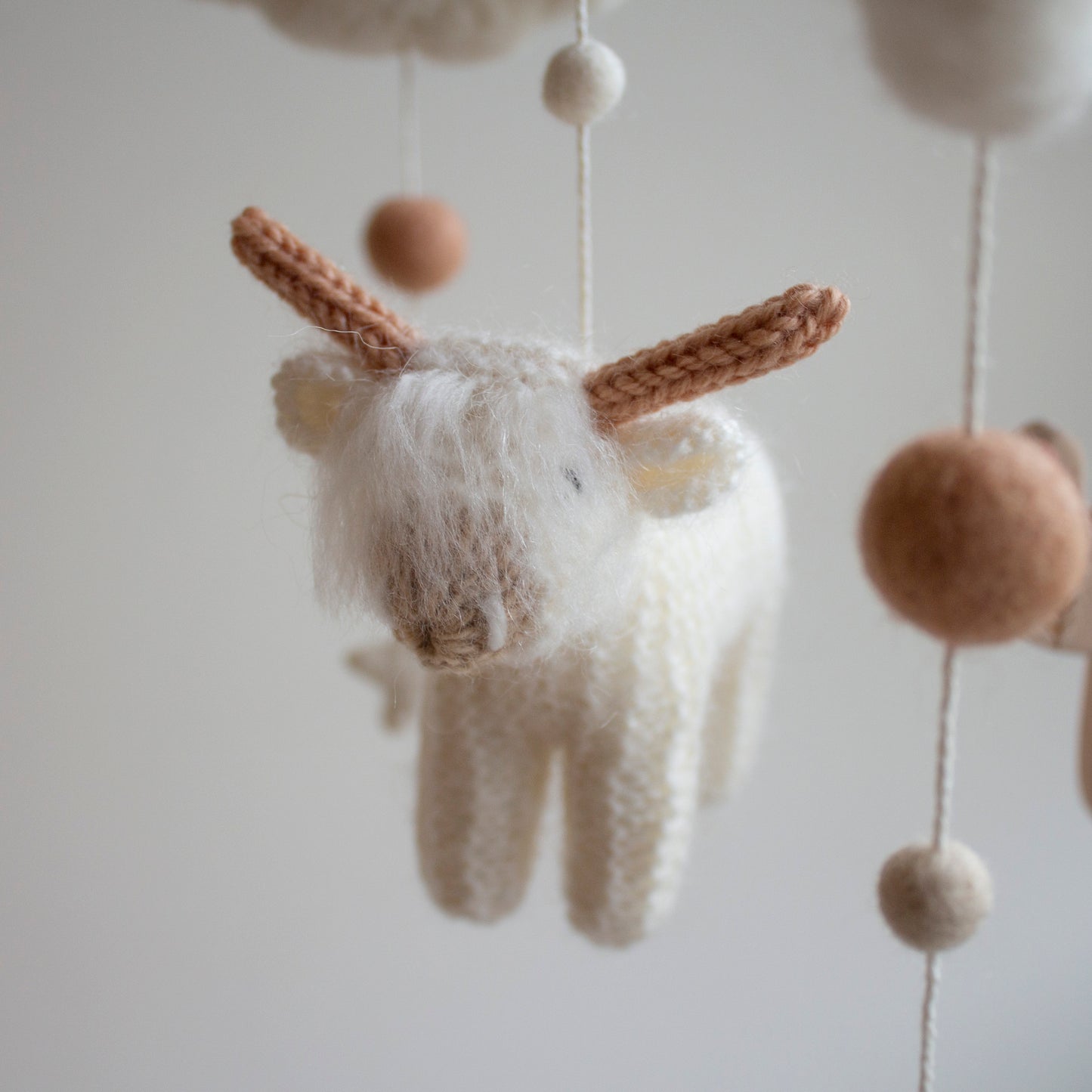 A close-up of the shaggy, fluffy white longhorn cow, highlighting the hand-knitted fringe and intricate detail. This "hairy coo" is made from premium wool yarn OEKO-TEX Standard 100 safe for newborns. This level of artisanship ensures the mobile remains a cherished heirloom gift for years to come. The soft textures and timeless design make it a standout feature of the mobile, which is suitable for different baby gifts and serves as a high-quality keepsake from Lanacrocheting.com.