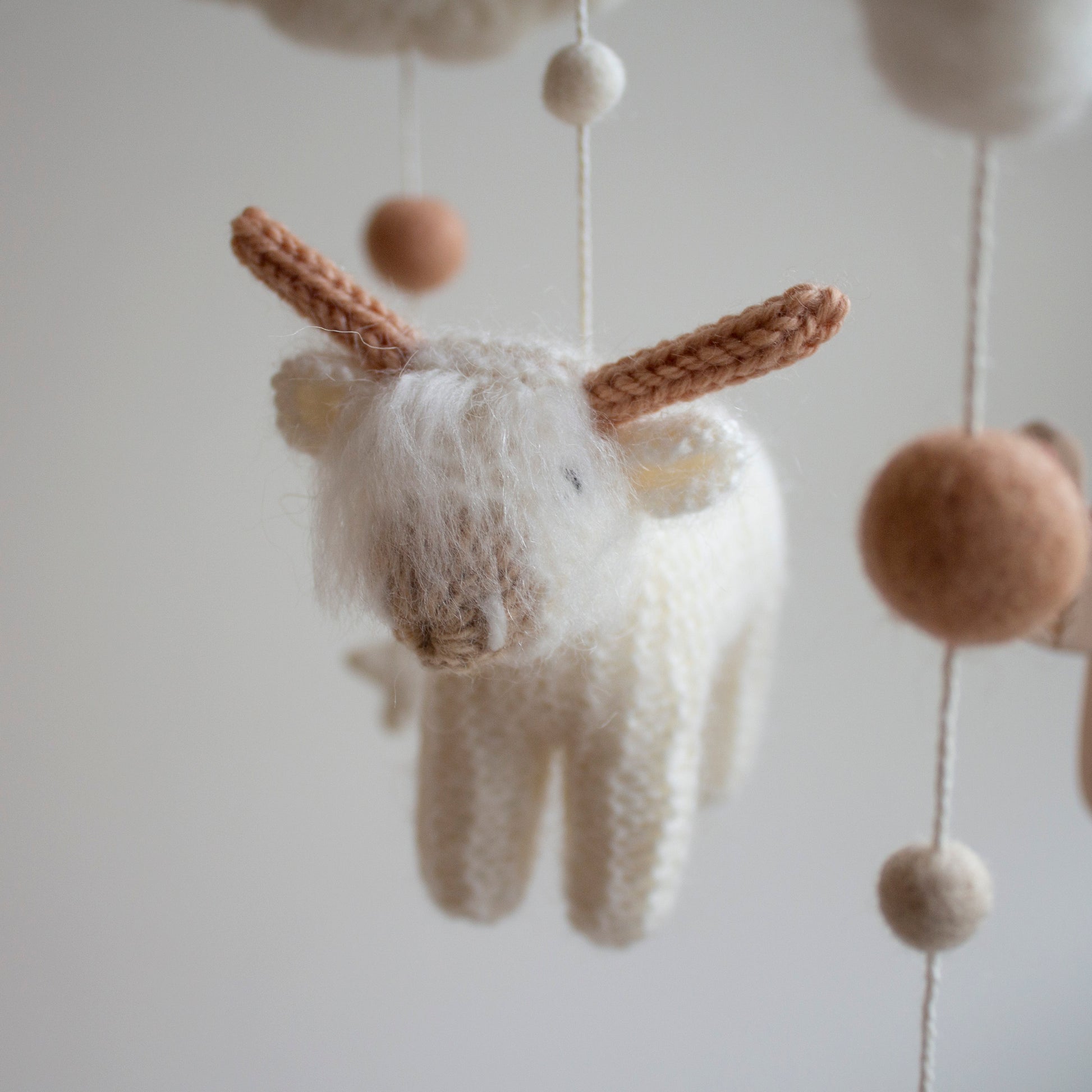 A close-up of the shaggy, fluffy white longhorn cow, highlighting the hand-knitted fringe and intricate detail. This "hairy coo" is made from premium wool yarn OEKO-TEX Standard 100 safe for newborns. This level of artisanship ensures the mobile remains a cherished heirloom gift for years to come. The soft textures and timeless design make it a standout feature of the mobile, which is suitable for different baby gifts and serves as a high-quality keepsake from Lanacrocheting.com.