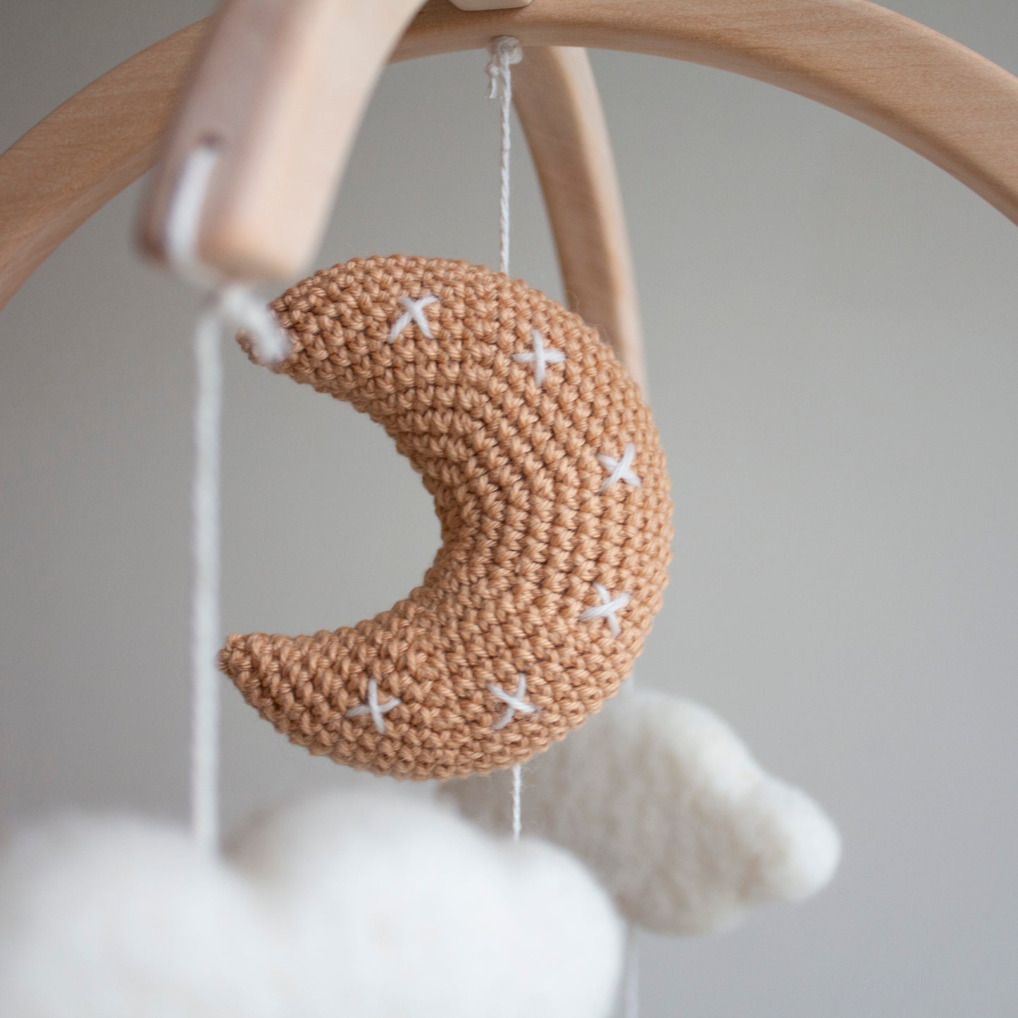 Close-up of the tan crochet moon featuring meticulous white cross-stitch details. Part of the White Longhorn Cow Mobile, it is individually crafted using wool yarn OEKO-TEX Standard 100 safe for infants. The moon hangs from a natural untreated solid wood mobile frame alongside untreated solid wood cactuses. This attention to detail defines its timeless design and value as an heirloom gift. Such quality craftsmanship makes the entire mobile suitable for different baby gifts and nursery themes.