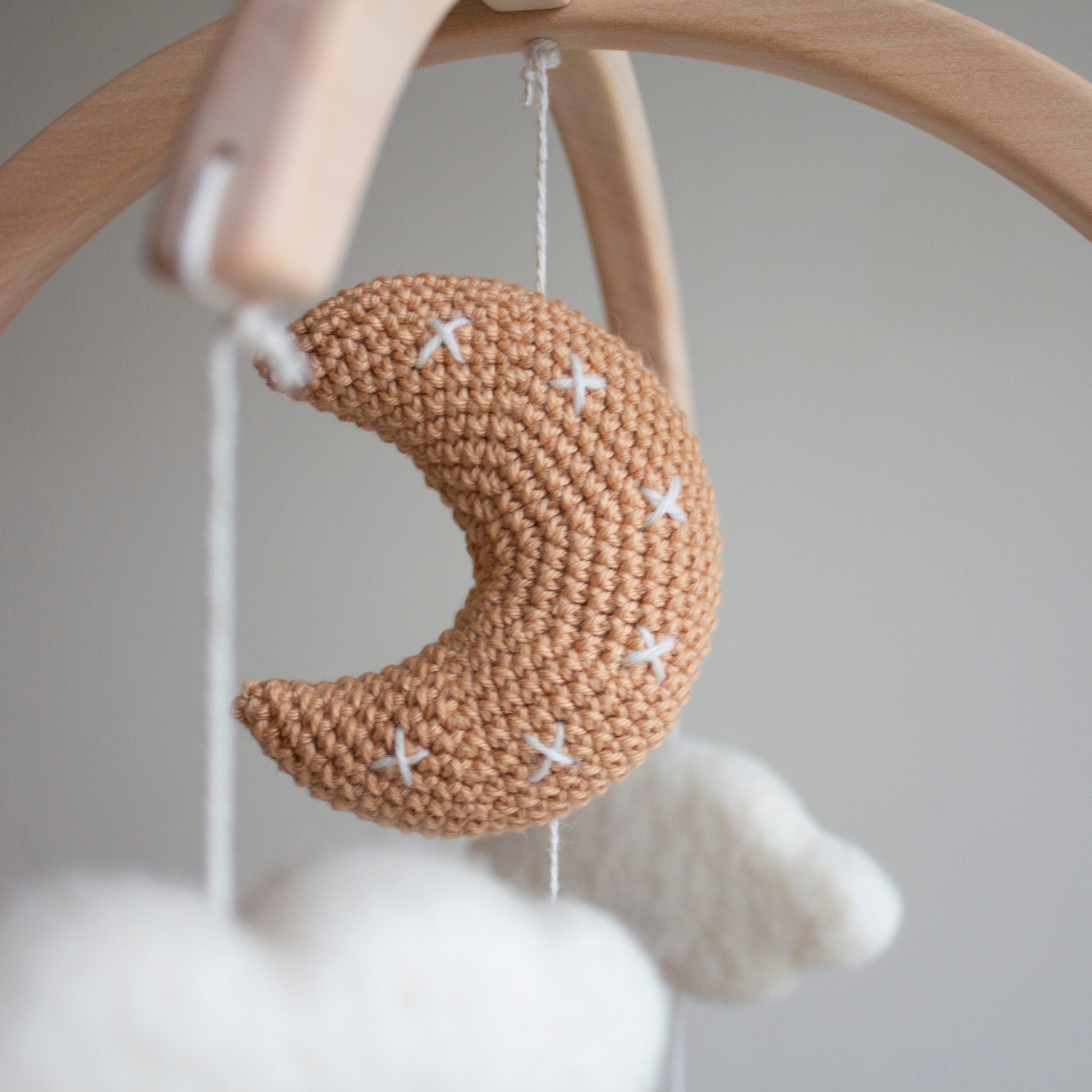 Close-up of the tan crochet moon featuring meticulous white cross-stitch details. Part of the White Longhorn Cow Mobile, it is individually crafted using wool yarn OEKO-TEX Standard 100 safe for infants. The moon hangs from a natural untreated solid wood mobile frame alongside untreated solid wood cactuses. This attention to detail defines its timeless design and value as an heirloom gift. Such quality craftsmanship makes the entire mobile suitable for different baby gifts and nursery themes.