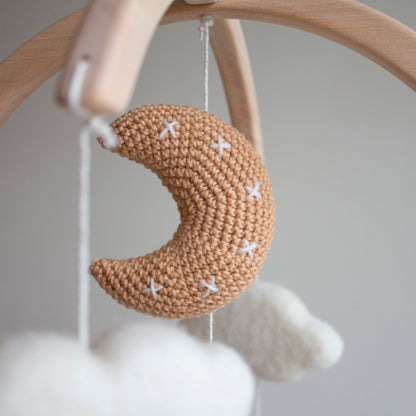 Close-up of the tan crochet moon featuring meticulous white cross-stitch details. Part of the White Longhorn Cow Mobile, it is individually crafted using wool yarn OEKO-TEX Standard 100 safe for infants. The moon hangs from a natural untreated solid wood mobile frame alongside untreated solid wood cactuses. This attention to detail defines its timeless design and value as an heirloom gift. Such quality craftsmanship makes the entire mobile suitable for different baby gifts and nursery themes.
