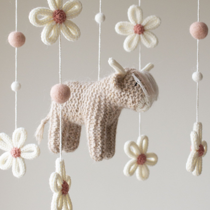 Close-up of a knitted highland cow in soft beige with fuzzy texture and ivory yarn horns.