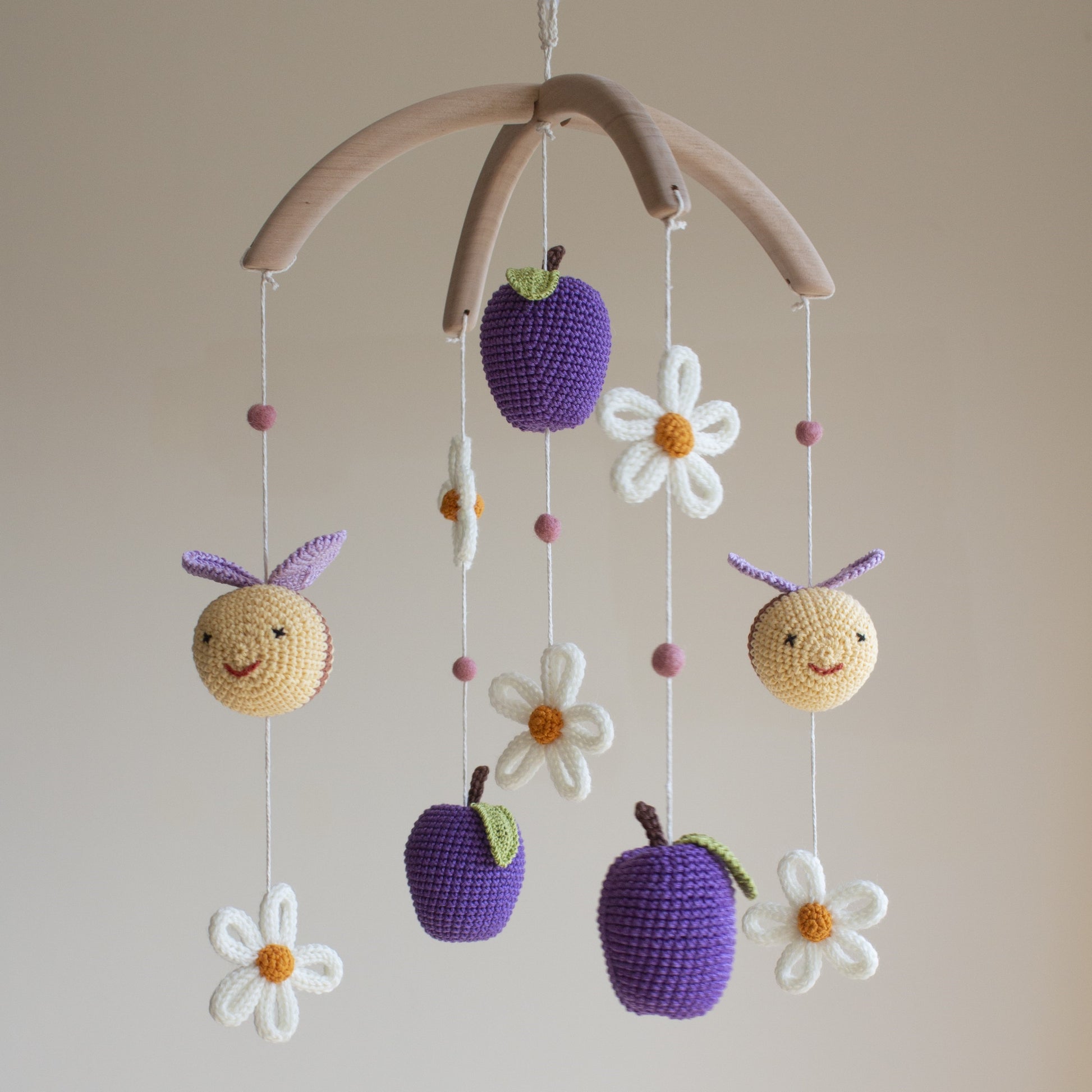 Close-up of a hand-crocheted bee with purple wings and golden-tan yarn for a garden nursery theme.