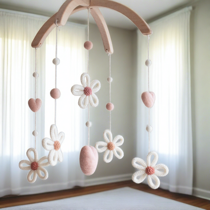 Hand-knitted daisy baby mobile in peachy blush and cream hanging in a modern white nursery.