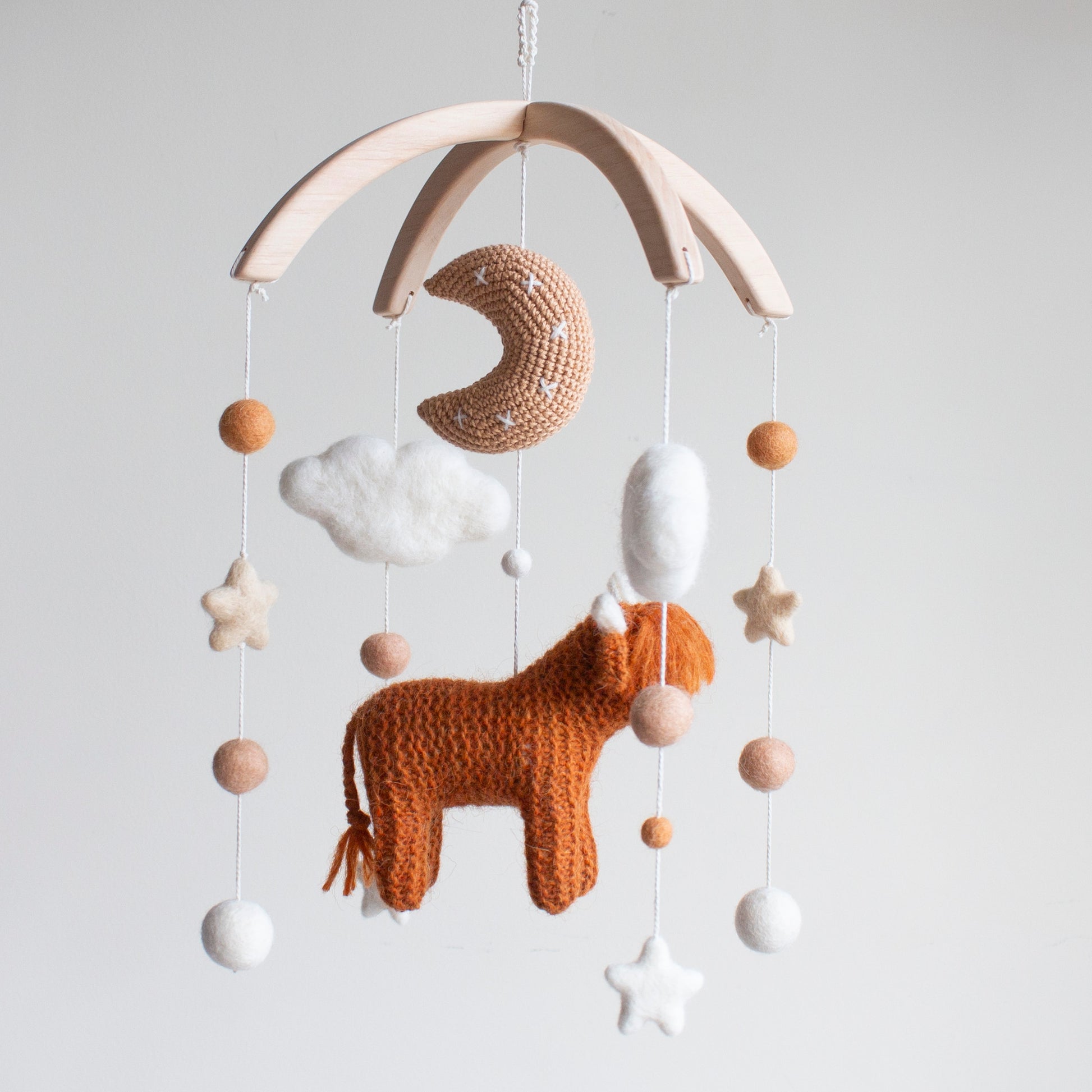 Gender-neutral baby mobile hanging above a wooden crib in a minimalist Scandi-style nursery.