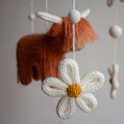 Detailed close-up of a hand-knitted ivory daisy and peachy-blush wool ball on a premium baby mobile. This shot highlights the delicate artisan stitching and soft textures that make our nursery decor a unique heirloom gift. Using 100% certified organic wool, we ensure a chemical-free environment for the nursery. Perfect for gift-givers looking for a definite upgrade to mass-market solutions that will be cherished as a lifelong childhood keepsake.