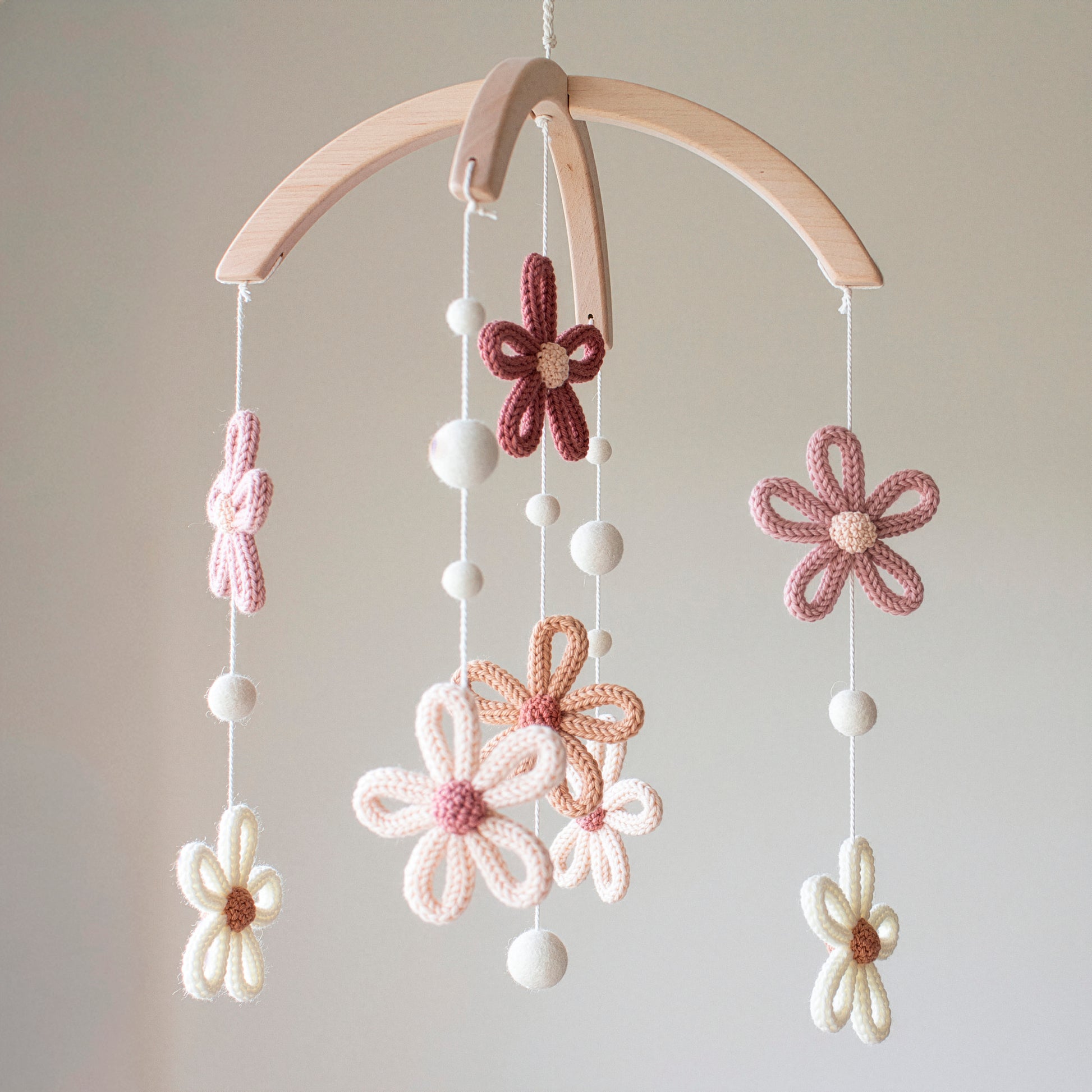 This charming nursery mobile features crochet flowers and felted white wool balls suspended from a cross-shaped wooden hanger. Using wool yarn OEKO-TEX Standard 100 safe for baby environments, it provides a safe, chemical-free atmosphere. The use of untreated solid wood highlights its eco-friendly nature. With its timeless design, this mobile is a top choice for those seeking an heirloom gift or unique baby shower presents that blend beautifully with modern nursery themes.