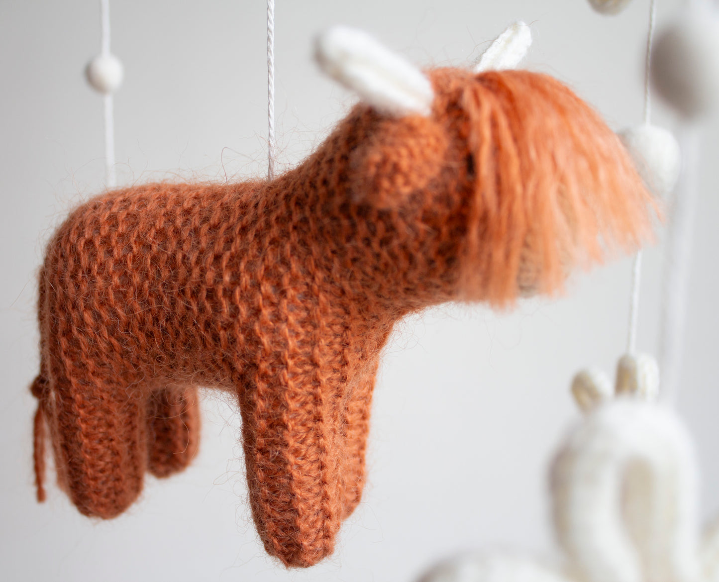 Close-up of an artisan hand-knitted highland cow in rich rust wool, showcasing the intricate texture and high-quality craftsmanship of LanaCrocheting. This macro shot highlights the premium materials and "slow-stitch" technique used in our Northern Ireland studio. By focusing on material integrity and artisan skill, we provide a vetted, safe, and prestigious nursery accessory that appeals to affluent gift-givers who avoid promotional impulse buys.