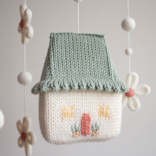 Close-up of a hand-knitted cottage with a sage green roof and floral embroidery for a cottagecore nursery.