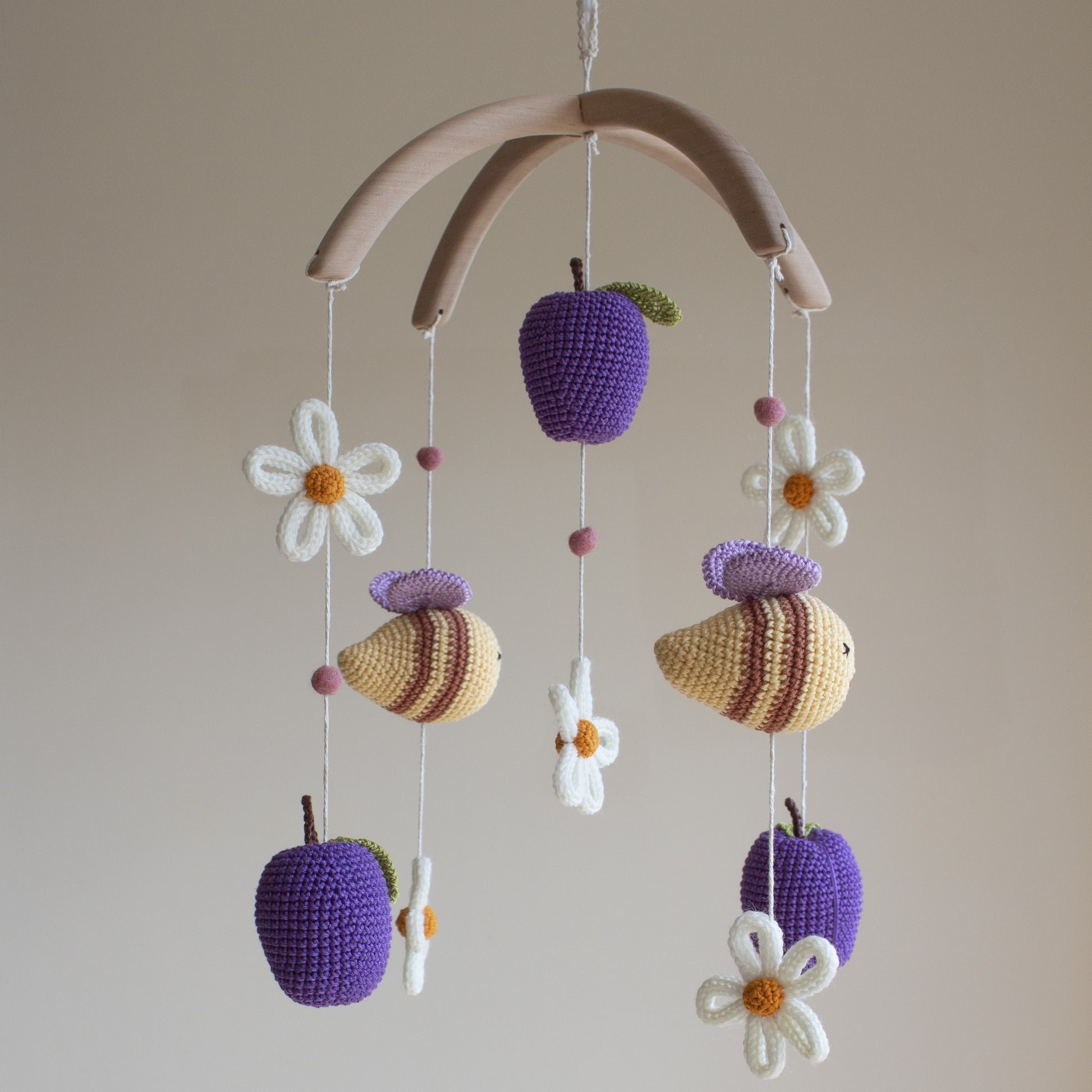 Detailed shot of a purple crochet plum with a green leaf and brown stem on a baby mobile.
