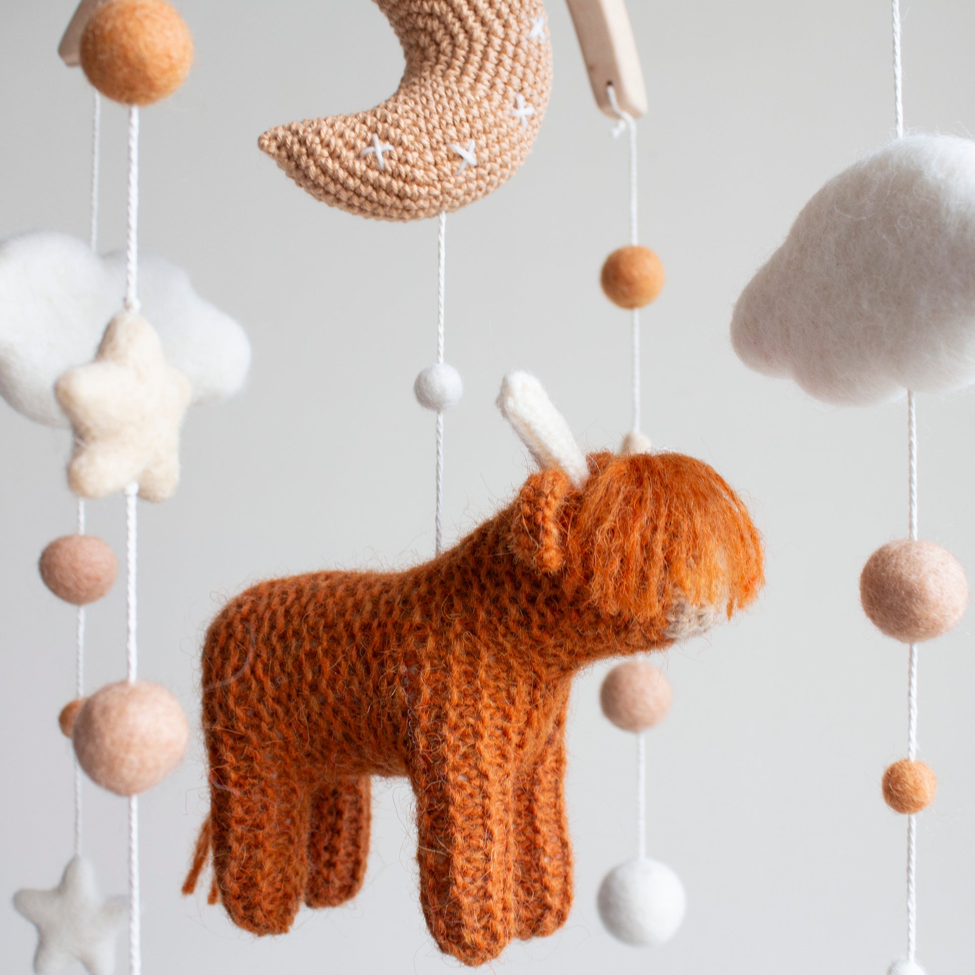 A close-up profile shot of the hand-knitted highland cow in a rich burnt orange color, showcasing its soft texture and detailed horns for a minimalist nursery.