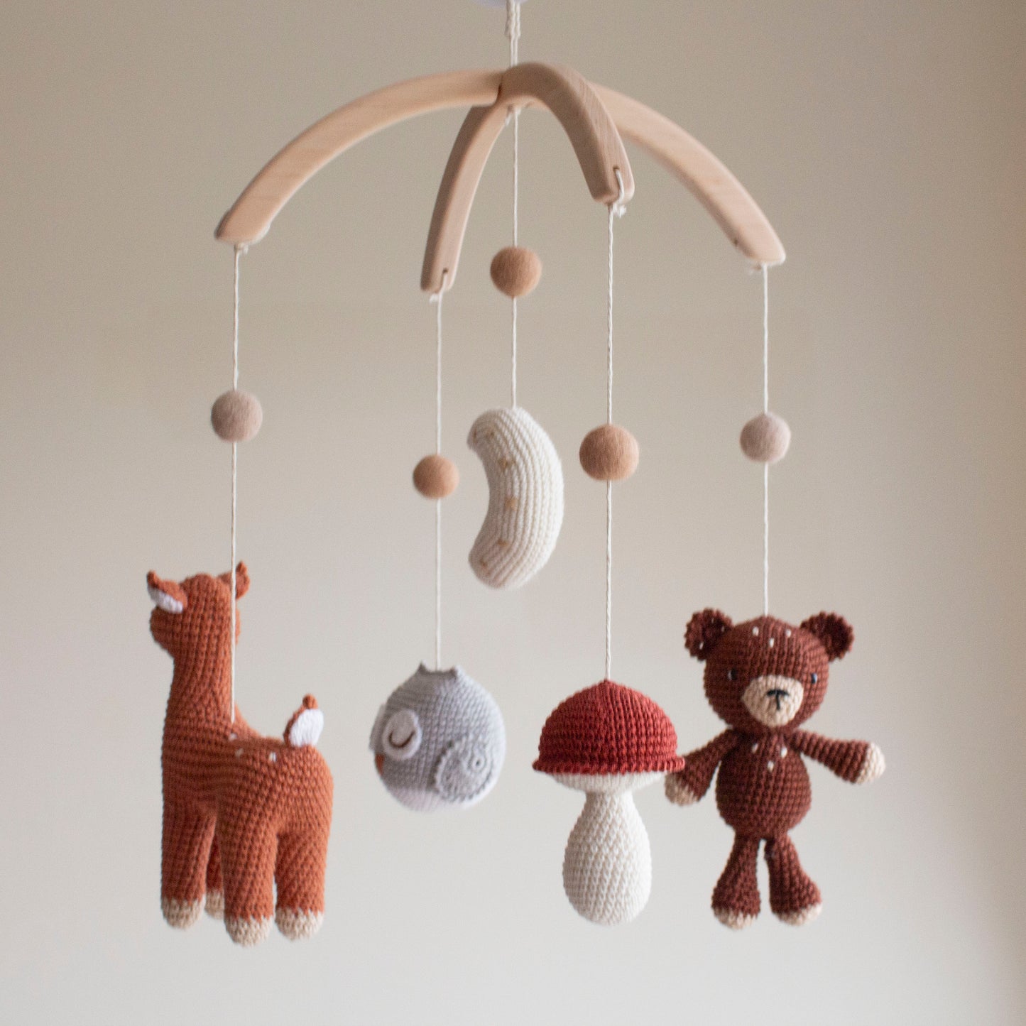 Close-up of a terracotta hand-crocheted deer with white spots for a woodland nursery theme. Macro view of a red-capped mushroom and neutral crochet moon on an artisan mobile.