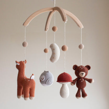 Close-up of a terracotta hand-crocheted deer with white spots for a woodland nursery theme. Macro view of a red-capped mushroom and neutral crochet moon on an artisan mobile.