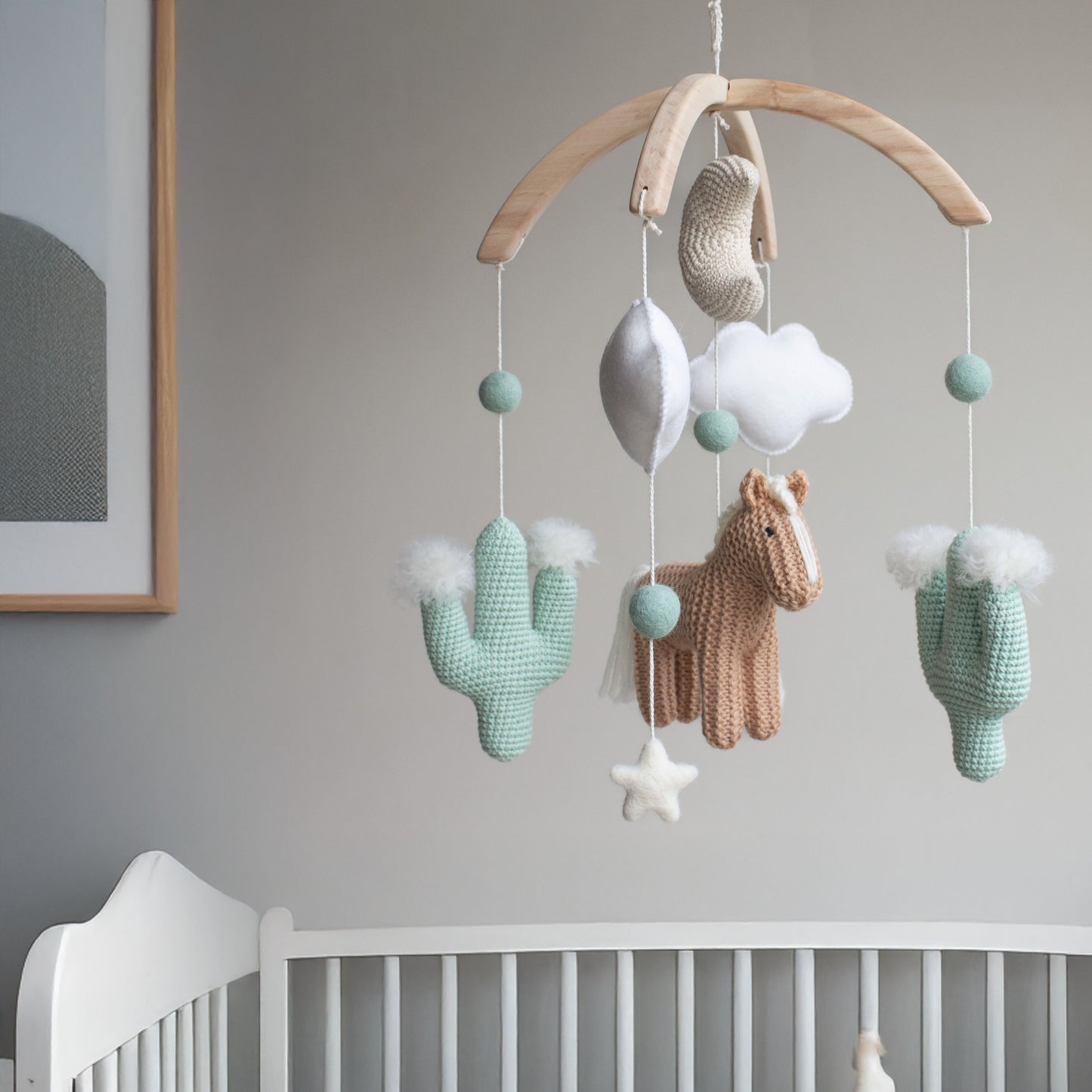 Artisan horse and cactus mobile hanging above a white wooden crib in a minimalist UK nursery with natural lighting. This visual demonstration of safety and scale shows the mobile as a central part of a gender-neutral "Heritage Farmyard" aesthetic. Perfectly styled to appeal to the expecting mum, this high-quality nursery art helps parents visualize their dreamy nursery while ensuring the product meets their high standards for vetted, safe, and sustainable decor.