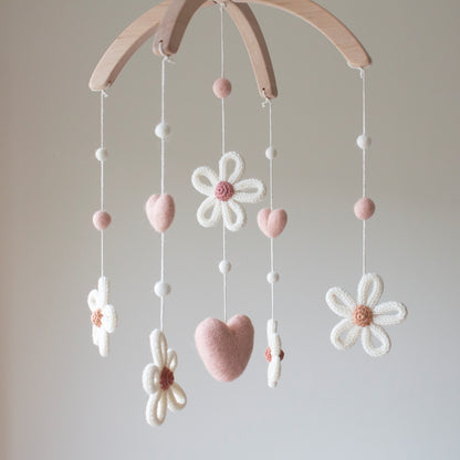 Hand-knitted peachy blush daisy with a dusty rose center and white wool petals. Soft wool hearts and felted balls in peachy blush and ivory on a floral nursery mobile.