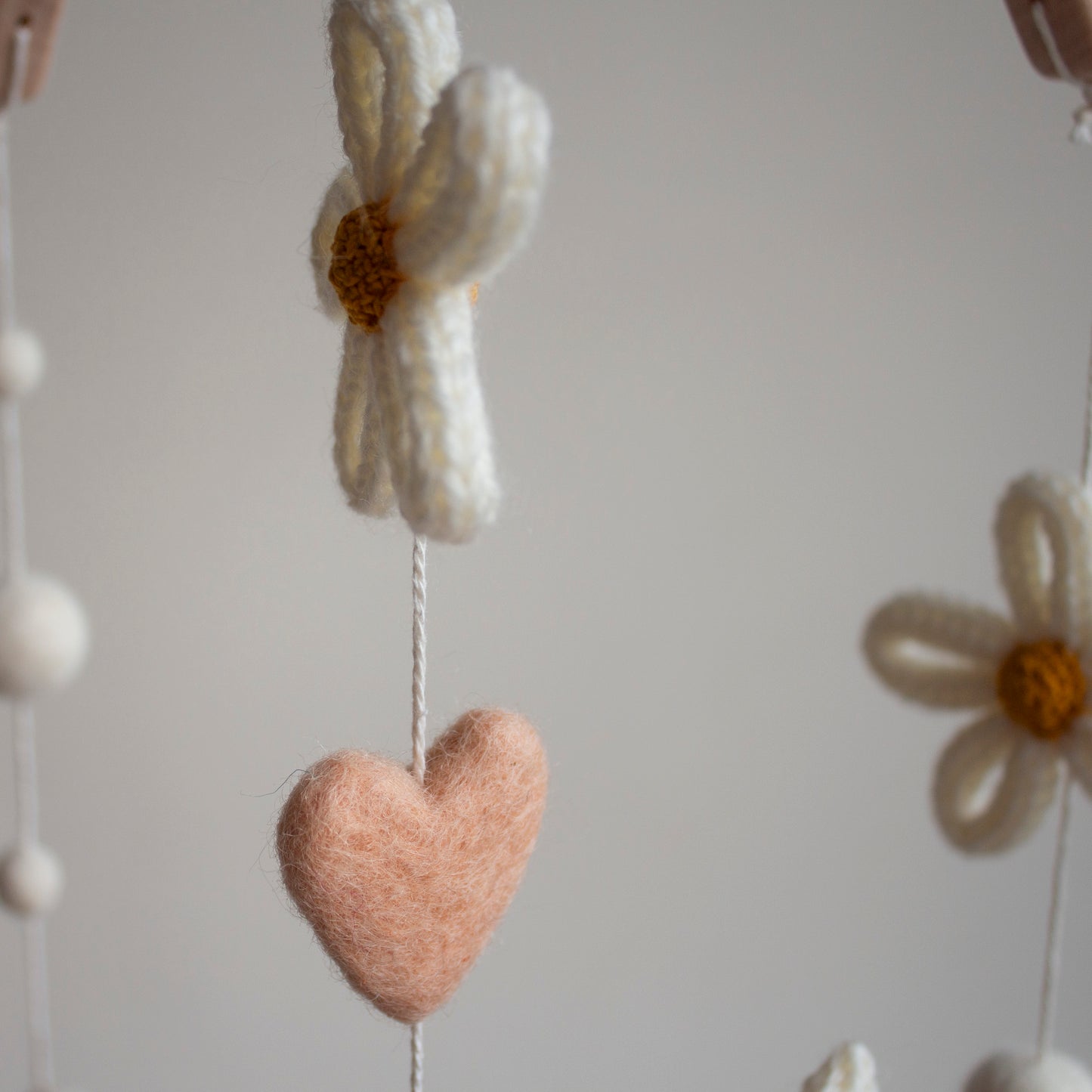 Close-up of a soft, peachy-blush wool heart and an ivory knitted daisy, representing the curated design aesthetics and non-toxic materials of LanaCrocheting. Hand-knitted in our Northern Ireland atelier, these details reflect a commitment to quality and safety. This artisan-level craftsmanship is designed for the high-end UK market, appealing to those who want a personalized, meaningful gift that supports small, ethical, and sustainable businesses.