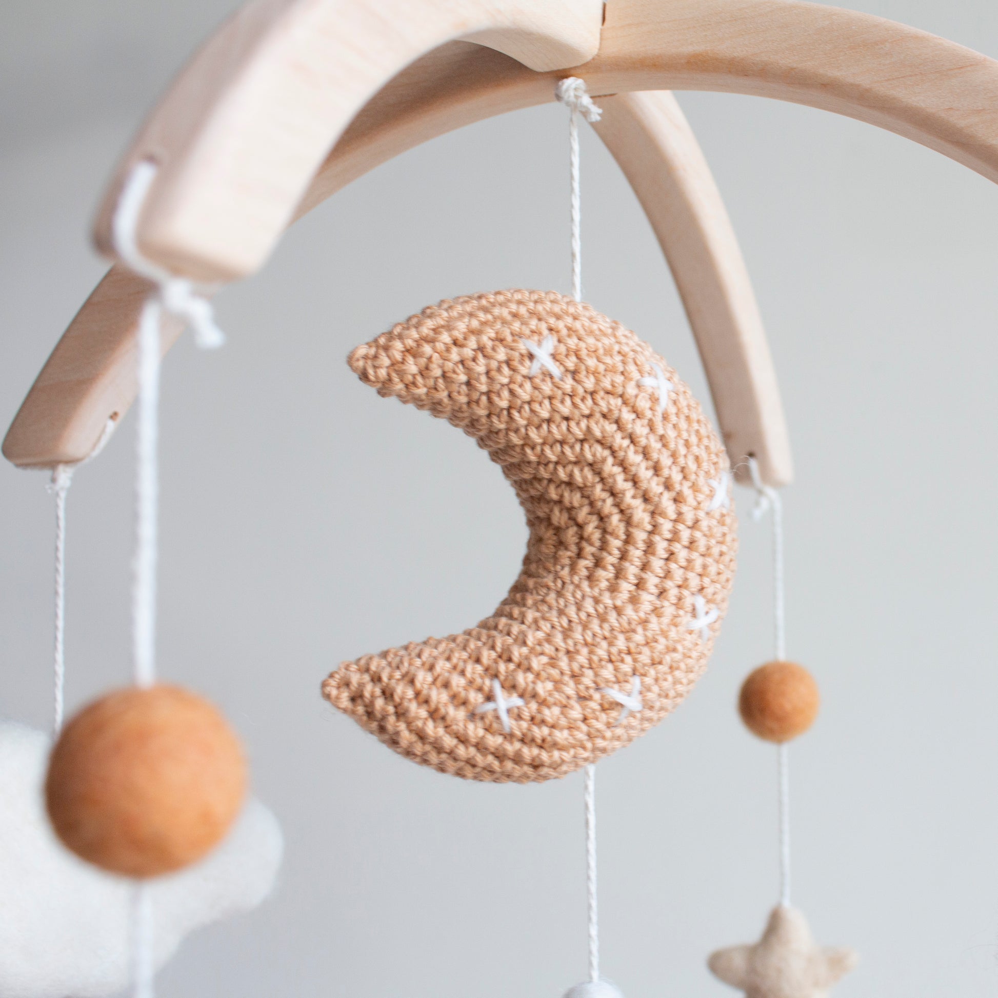 Crochet tan crescent moon and ivory wool stars hanging from a natural wood mobile frame.